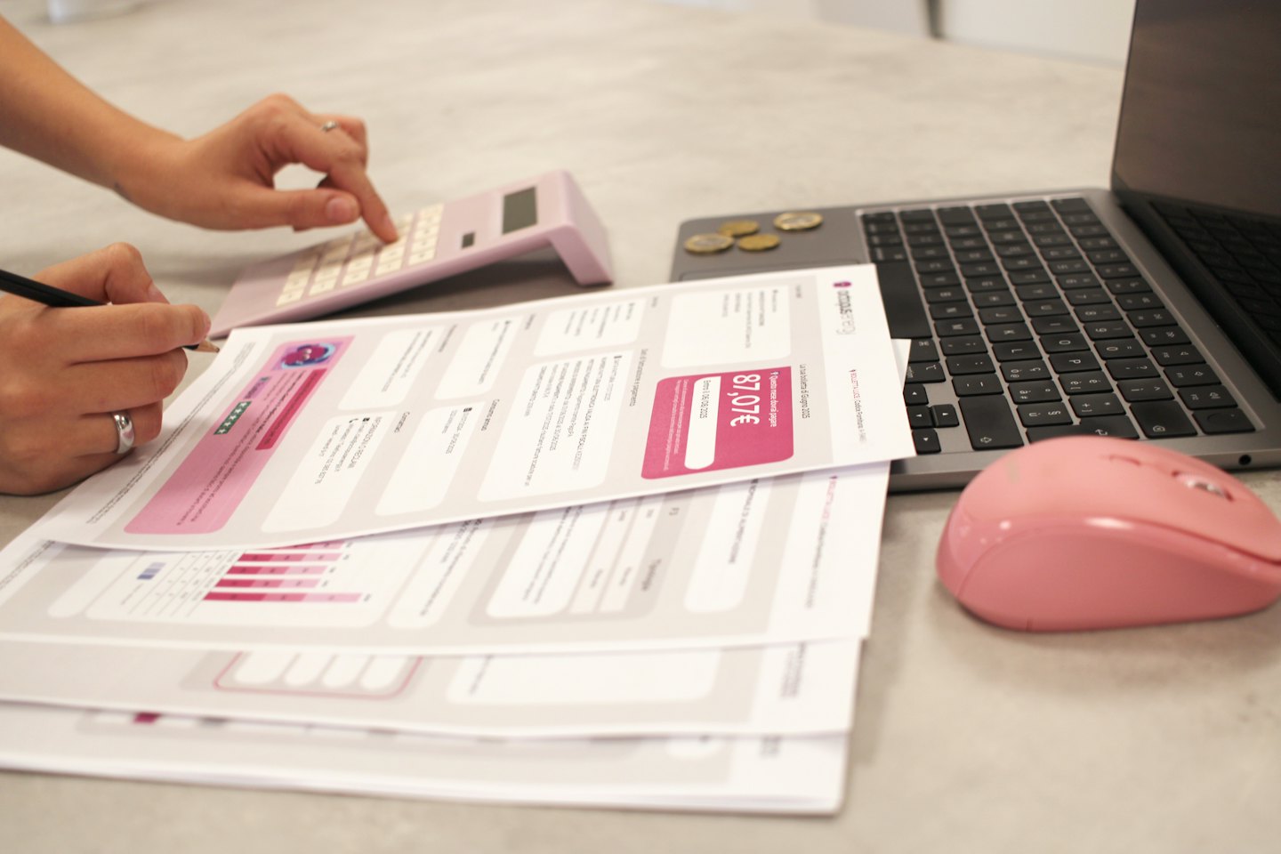 Persona che esamina documenti finanziari con una calcolatrice rosa e un laptop.